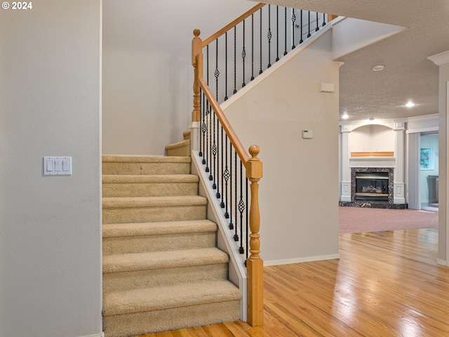 stairs with hardwood / wood-style flooring, a premium fireplace, a textured ceiling, and ornate columns