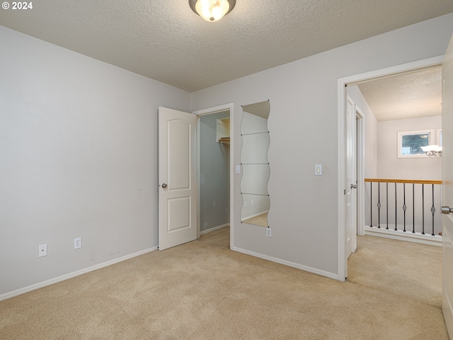 unfurnished bedroom featuring light colored carpet, a spacious closet, a textured ceiling, and a closet