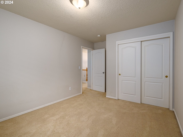 unfurnished bedroom featuring a textured ceiling, light carpet, and a closet