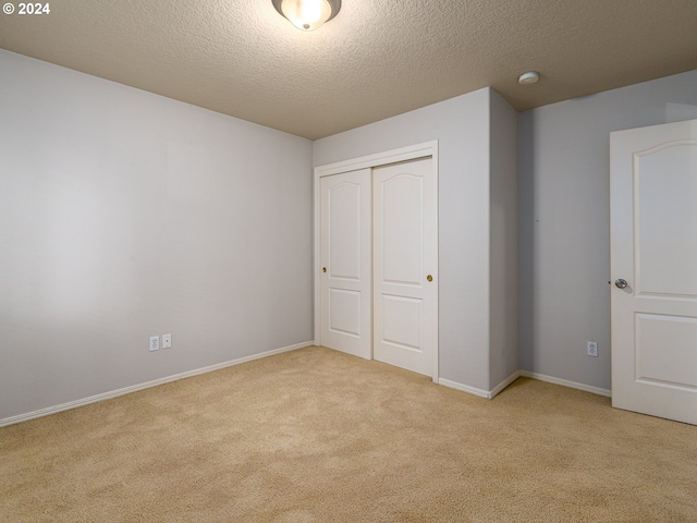 unfurnished bedroom featuring light carpet, a closet, and a textured ceiling