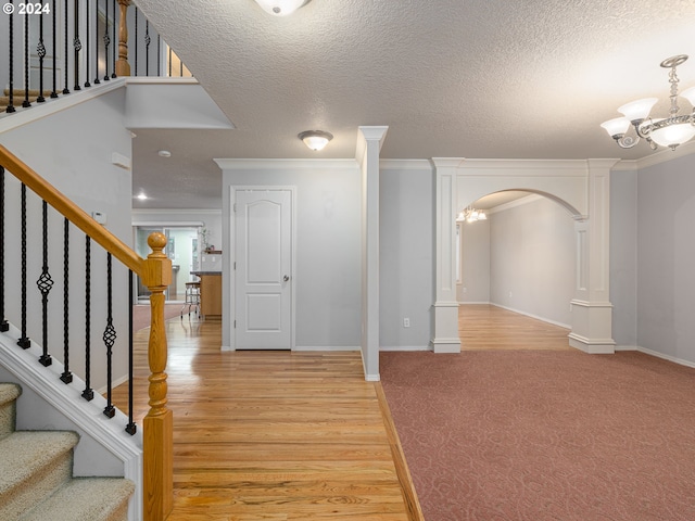 entrance foyer with a textured ceiling, light wood-type flooring, an inviting chandelier, and ornamental molding