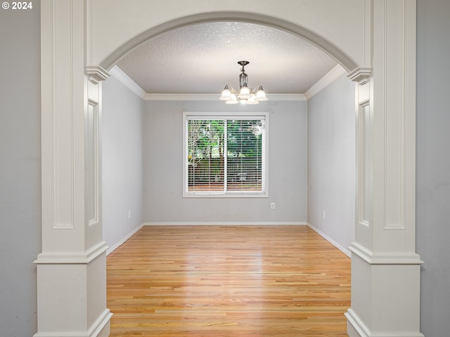 unfurnished room with decorative columns, a chandelier, a textured ceiling, and light wood-type flooring