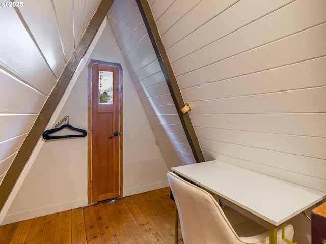 unfurnished office with light wood-type flooring, vaulted ceiling, and wooden walls