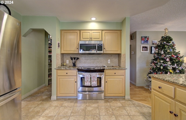 kitchen featuring light stone countertops, light brown cabinetry, a textured ceiling, stainless steel appliances, and light tile patterned floors