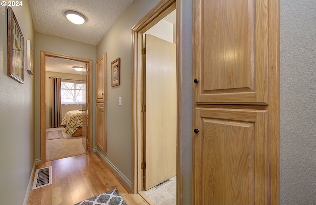 hallway with light hardwood / wood-style floors and a textured ceiling