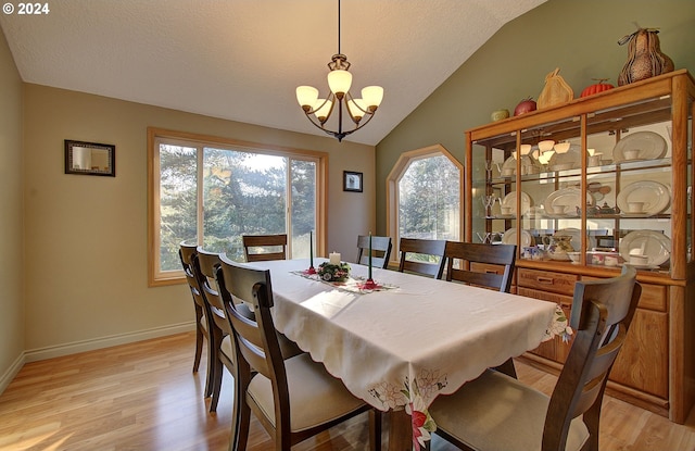 dining space with a notable chandelier, light wood-type flooring, a wealth of natural light, and lofted ceiling