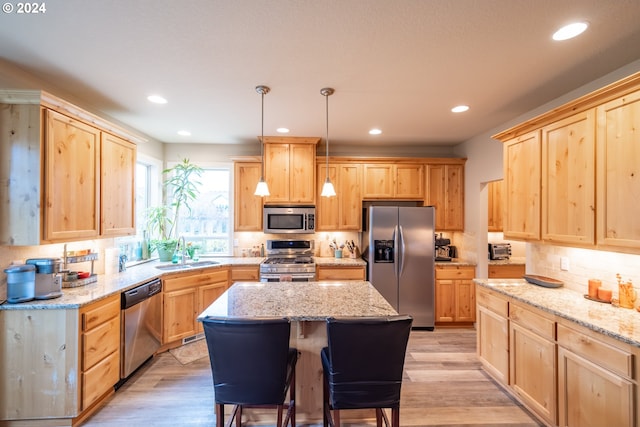 kitchen with a center island, hanging light fixtures, sink, appliances with stainless steel finishes, and light hardwood / wood-style floors