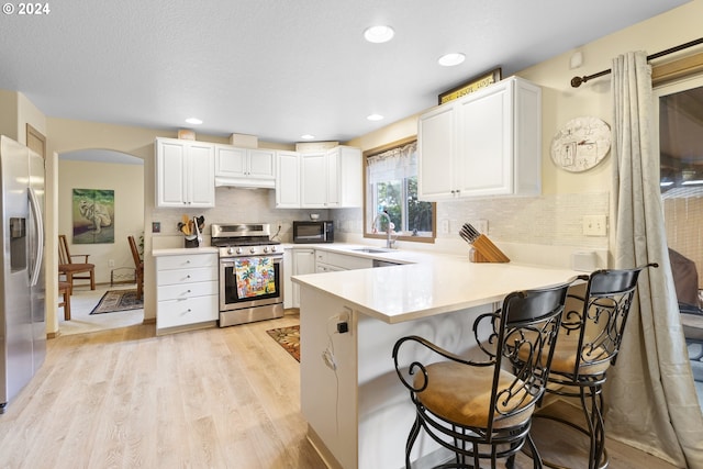 kitchen with white cabinets, kitchen peninsula, stainless steel appliances, light wood-type flooring, and a kitchen bar