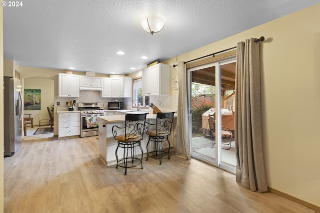 kitchen featuring light hardwood / wood-style floors, white cabinetry, kitchen peninsula, stainless steel appliances, and a kitchen bar