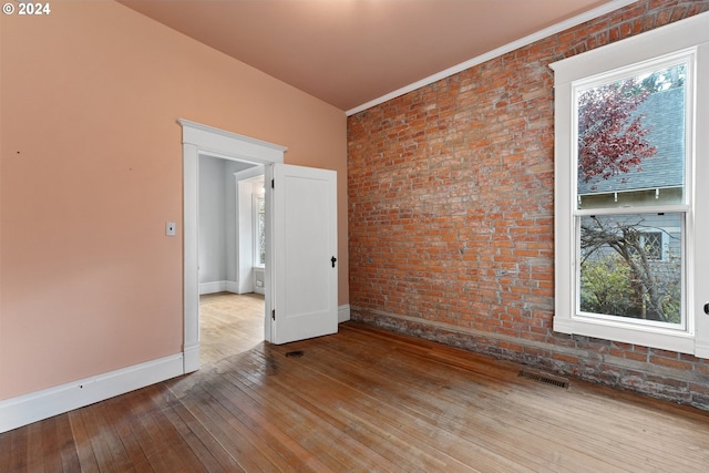 unfurnished room featuring brick wall and hardwood / wood-style floors