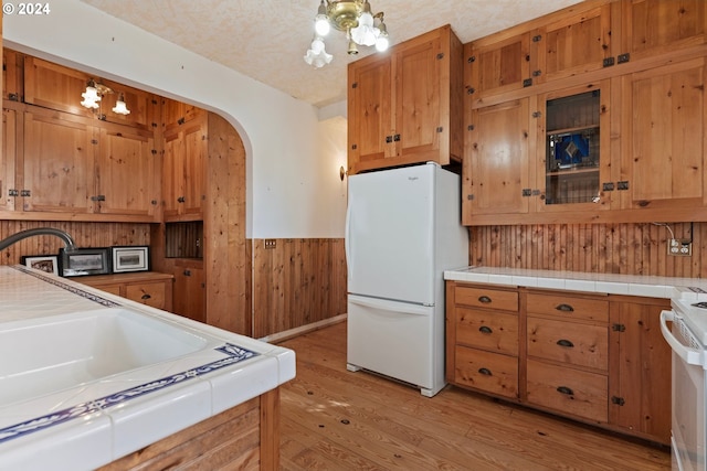 kitchen with tile countertops, wooden walls, light wood-type flooring, a textured ceiling, and white appliances