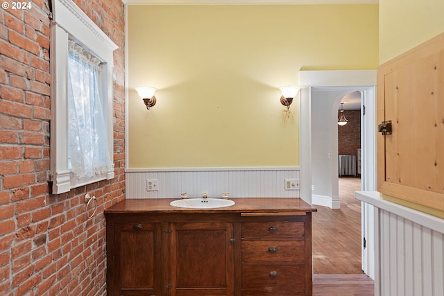 bathroom with vanity, brick wall, hardwood / wood-style flooring, and radiator