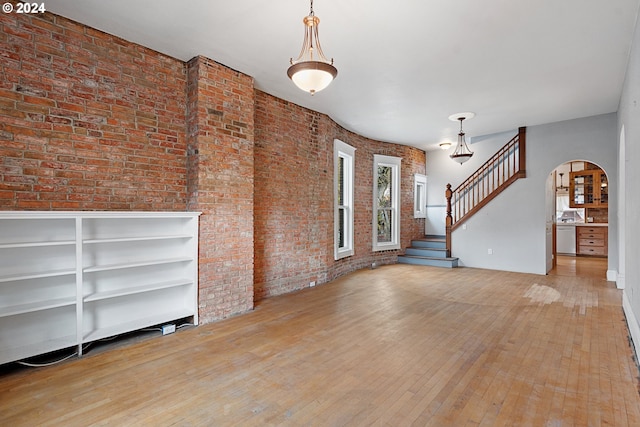 unfurnished living room featuring brick wall and light wood-type flooring