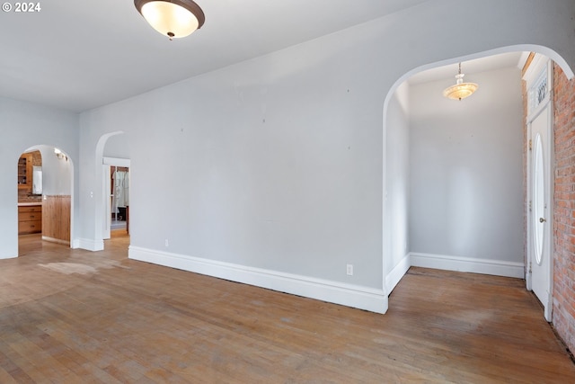 empty room with brick wall and hardwood / wood-style flooring