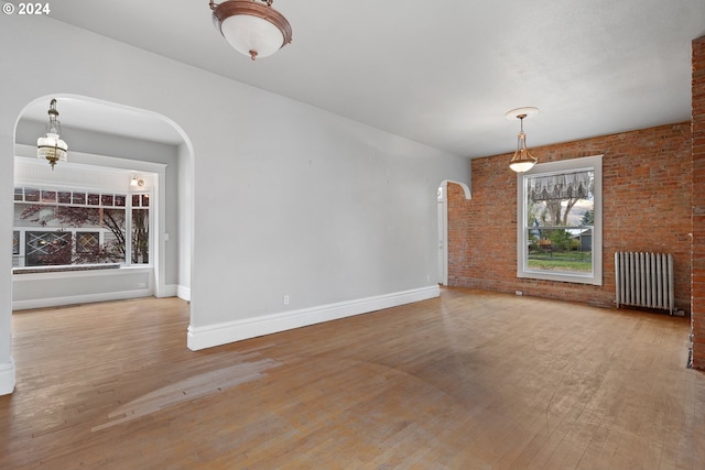 unfurnished living room with brick wall, wood-type flooring, and radiator