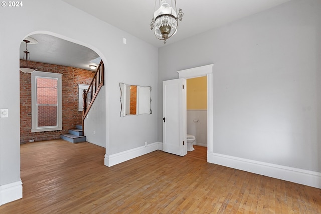 spare room featuring an inviting chandelier, hardwood / wood-style flooring, and brick wall