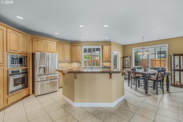 kitchen featuring appliances with stainless steel finishes, a kitchen island, light brown cabinets, a kitchen bar, and sink