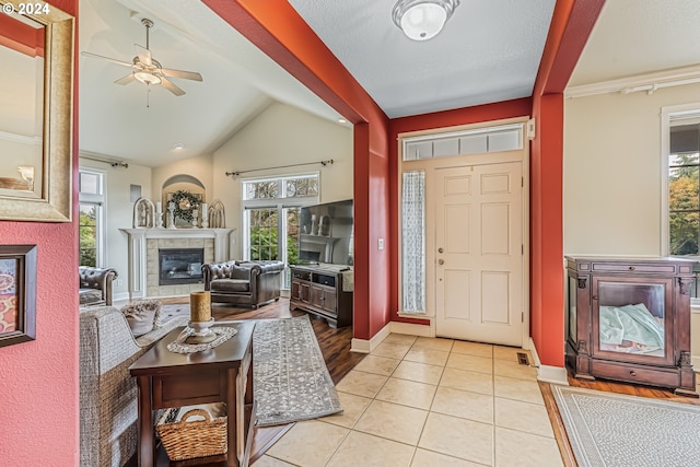 tiled foyer entrance featuring ceiling fan, a textured ceiling, lofted ceiling, and a tiled fireplace