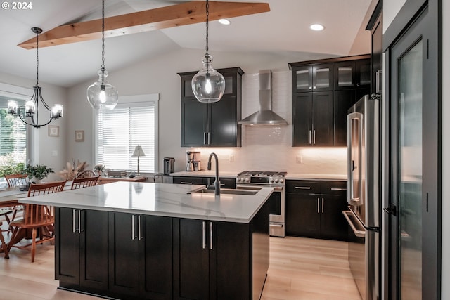 kitchen with pendant lighting, wall chimney range hood, stainless steel appliances, and a center island with sink