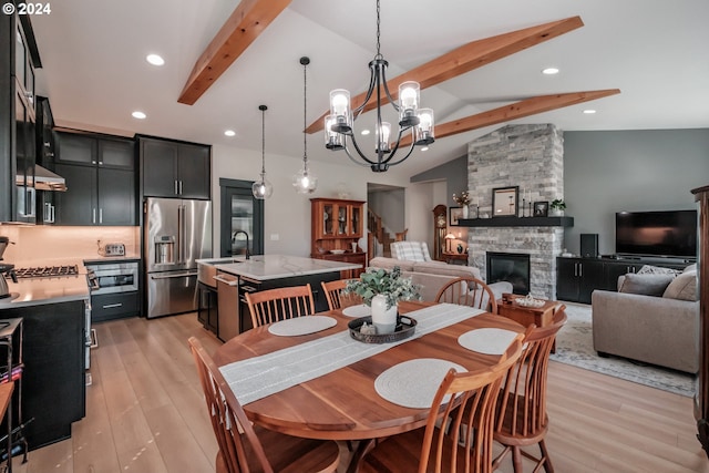 dining area with sink, a fireplace, lofted ceiling with beams, and light hardwood / wood-style floors