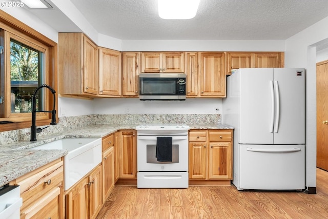 kitchen featuring a textured ceiling, sink, white appliances, and light hardwood / wood-style flooring