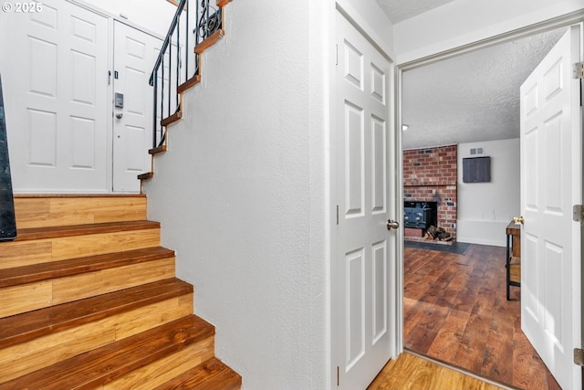 staircase with hardwood / wood-style flooring, a textured ceiling, and a brick fireplace