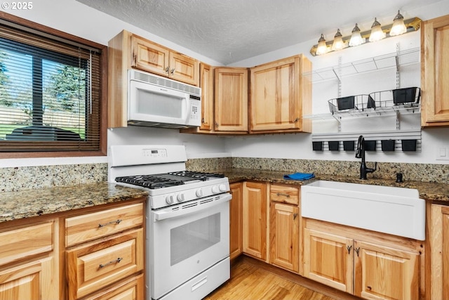 kitchen featuring white appliances, light hardwood / wood-style floors, dark stone counters, and sink