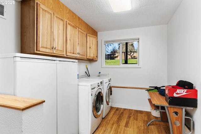 clothes washing area with cabinets, a textured ceiling, light hardwood / wood-style floors, and washer and dryer