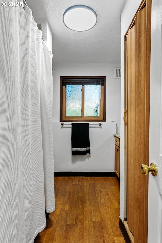 hallway with light wood-type flooring and a textured ceiling