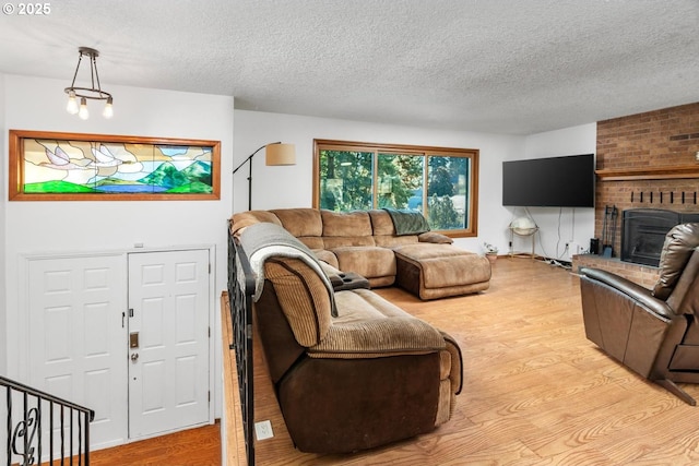 living room featuring light hardwood / wood-style flooring, a textured ceiling, and a brick fireplace