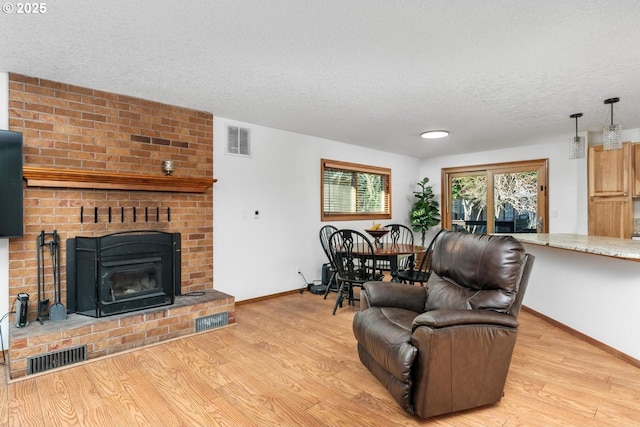 living room with light hardwood / wood-style flooring, a textured ceiling, and a brick fireplace