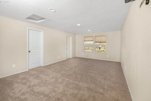 spare room featuring a textured ceiling, carpet, attic access, and baseboards