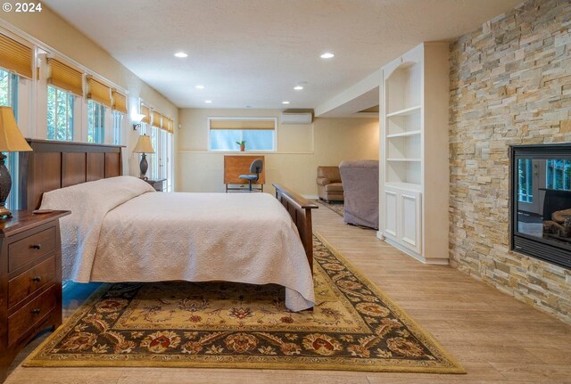 bedroom featuring a stone fireplace, a wall mounted air conditioner, and light hardwood / wood-style floors