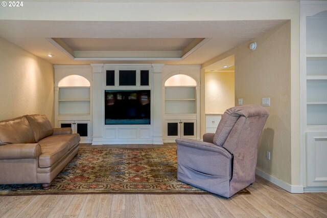 living room featuring built in shelves, a tray ceiling, and wood-type flooring