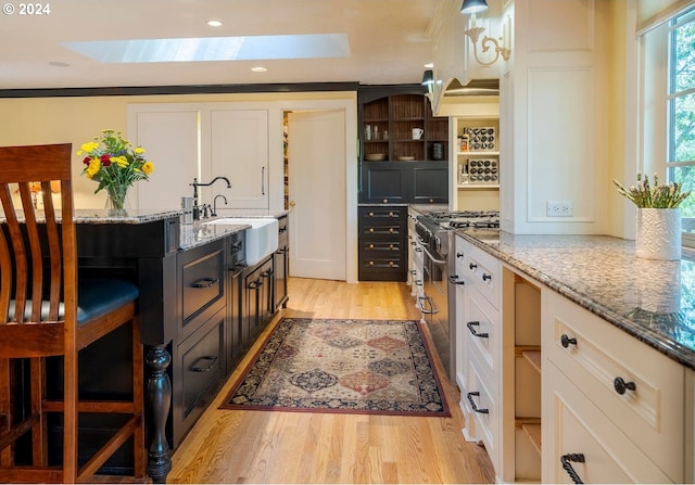 kitchen with light stone countertops, a skylight, white cabinets, and high end stainless steel range oven