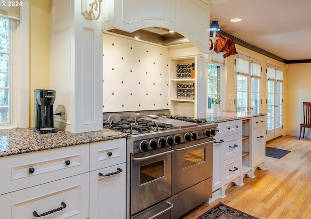 kitchen with high end stainless steel range, white cabinets, light stone countertops, and light hardwood / wood-style floors