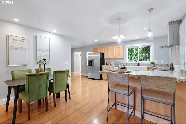 kitchen featuring light wood-type flooring, exhaust hood, kitchen peninsula, hanging light fixtures, and stainless steel refrigerator with ice dispenser