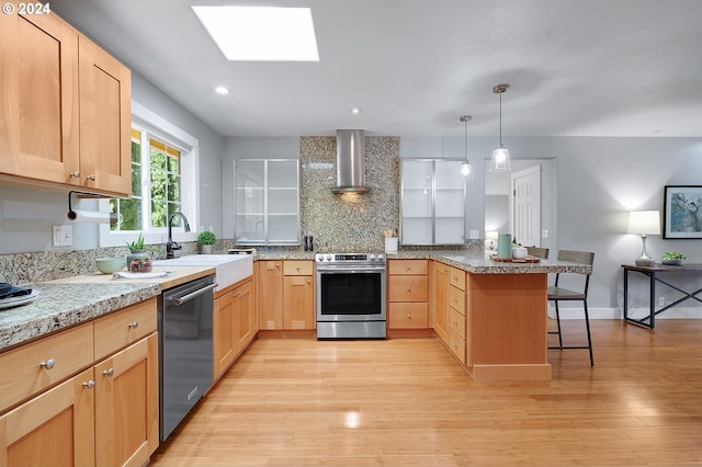 kitchen featuring wall chimney exhaust hood, light hardwood / wood-style flooring, dishwasher, a breakfast bar area, and stainless steel electric range oven