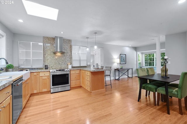 kitchen featuring pendant lighting, kitchen peninsula, light hardwood / wood-style flooring, appliances with stainless steel finishes, and light brown cabinetry