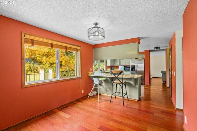 kitchen with a textured ceiling, light wood-style flooring, a peninsula, a breakfast bar, and stainless steel refrigerator with ice dispenser