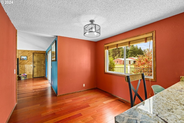 dining area with wood-type flooring, a textured ceiling, an inviting chandelier, and lofted ceiling