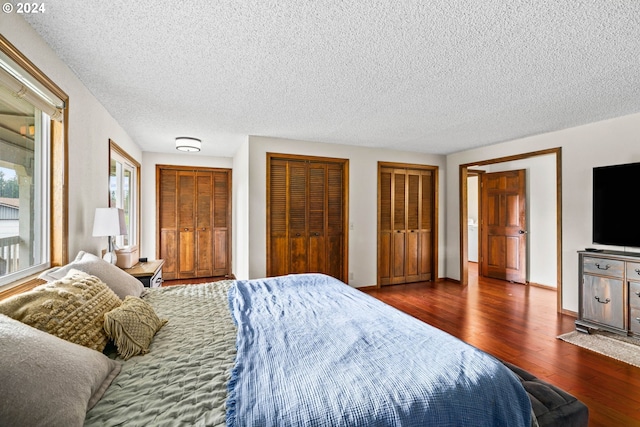 bedroom with a textured ceiling, dark hardwood / wood-style flooring, and two closets