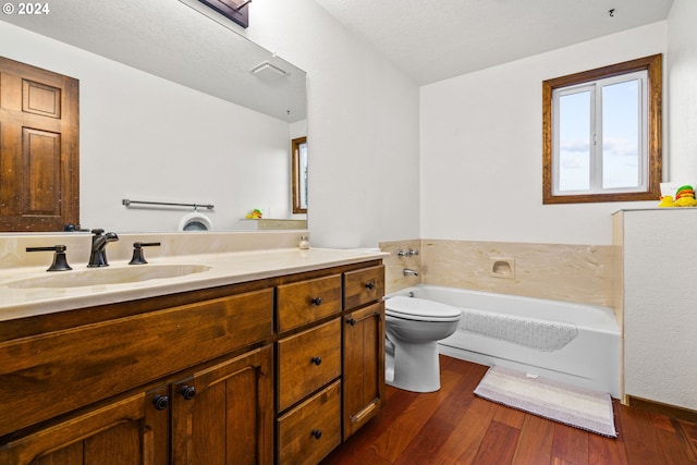 bathroom featuring vanity, a textured ceiling, a bath, wood-type flooring, and toilet