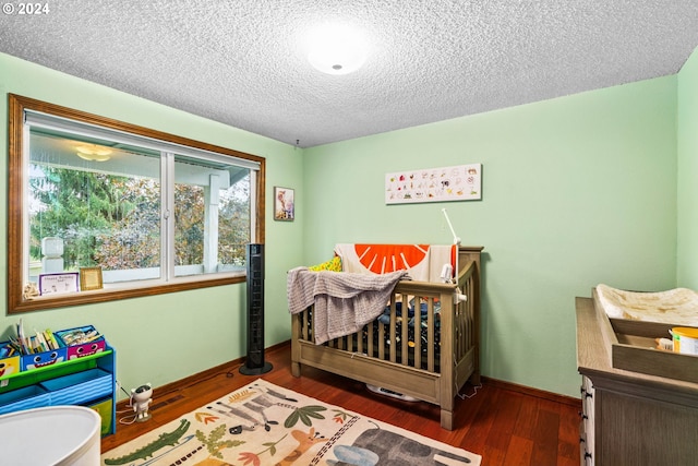 bedroom featuring a crib, a textured ceiling, and dark hardwood / wood-style floors