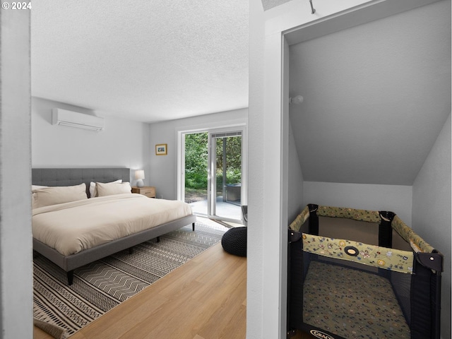 bedroom featuring access to exterior, wood-type flooring, a textured ceiling, and a wall mounted AC