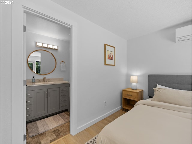 bedroom featuring a wall mounted air conditioner, ensuite bath, a textured ceiling, sink, and light hardwood / wood-style flooring