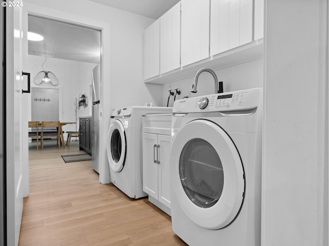 laundry room featuring cabinets, light wood-type flooring, and washing machine and clothes dryer