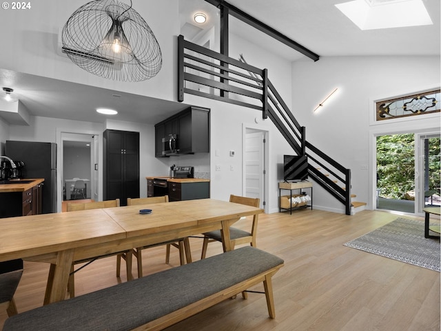 dining area featuring high vaulted ceiling, sink, light hardwood / wood-style flooring, a skylight, and beam ceiling