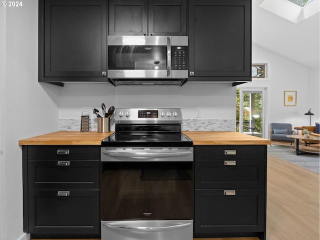 kitchen featuring butcher block countertops, light hardwood / wood-style flooring, stainless steel appliances, and vaulted ceiling