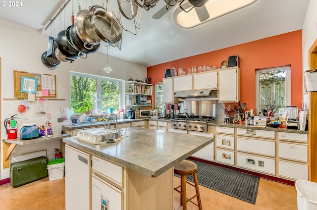 kitchen with ceiling fan, appliances with stainless steel finishes, white cabinetry, a center island, and a kitchen bar